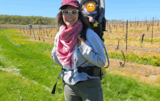 Victoria with a hiking backpack on outside in a bright sunny field with empty vines in the background.